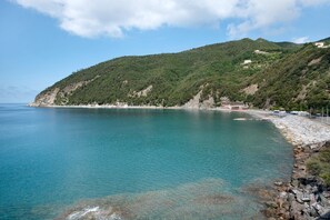 A coastal landscape with a clear view of the sea, a rocky shoreline, and a hill with buildings.