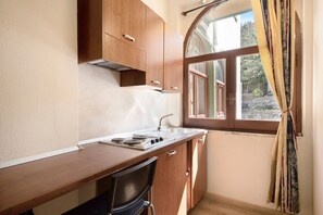 Une cuisine de taille réduite, dotée d’une fenêtre, de meubles en bois, d’un plan de travail et d’une chaise.