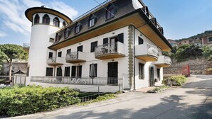 Un hotel de varios pisos con balcones, un patio central y un muro de piedra al fondo.