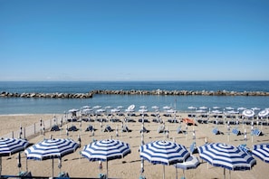 A beach with rows of blue and white striped umbrellas and lounge chairs, a rocky breakwater, and calm sea. - Studio Apartment Moneglia 35 near the beach with shared pool and Wi-Fi (Moneglia)