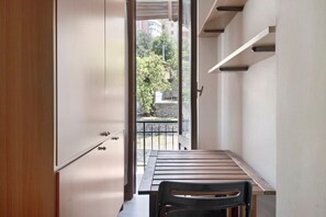 Un pasillo estrecho con una puerta de madera, un banco y vistas a un balcón con barandilla.
