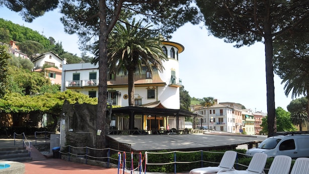Un edifici amb terrassa, una palmera i una filera de seients blans per relaxar-se.