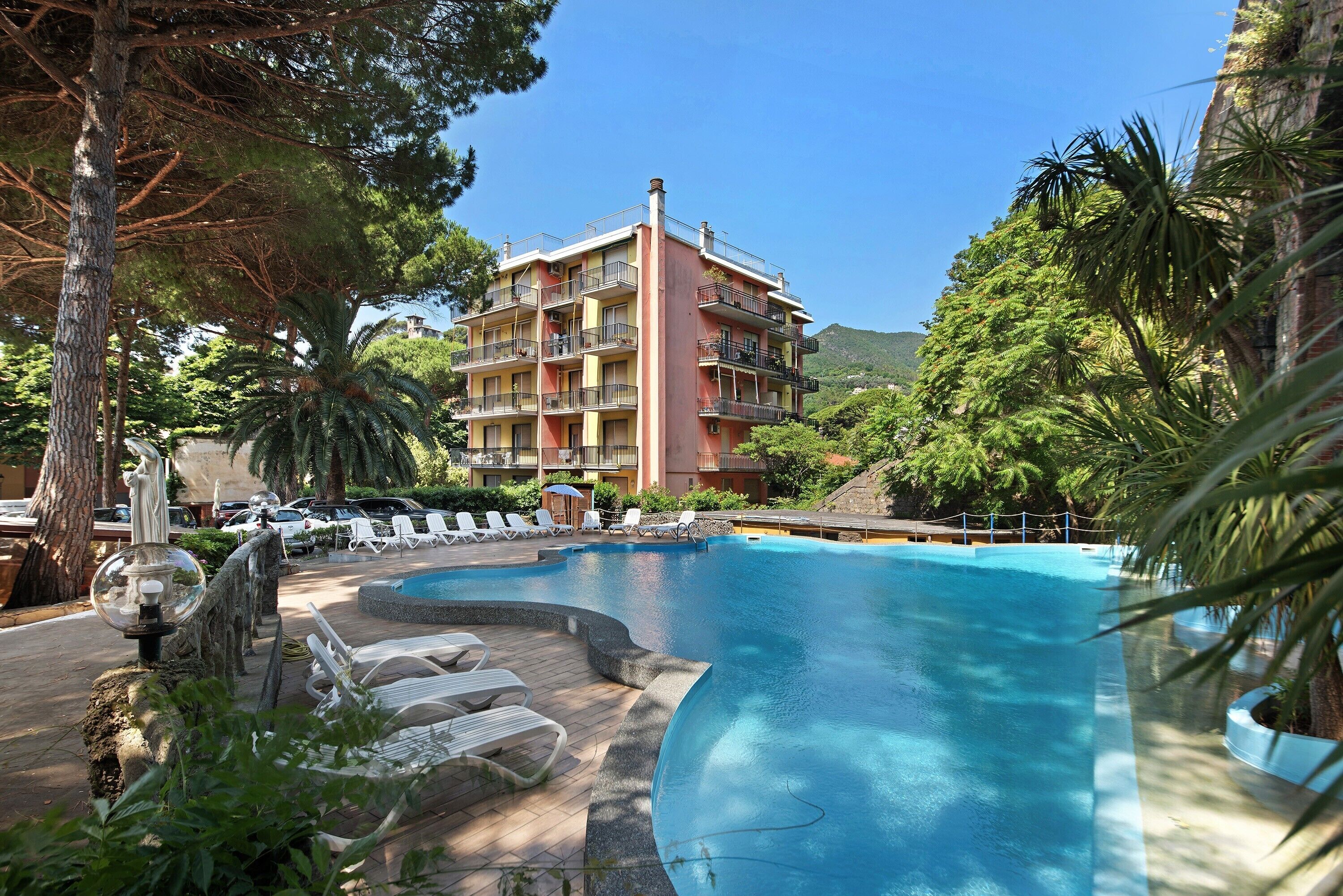 A hotel with a swimming pool, lounge chairs, and a mountainous backdrop.