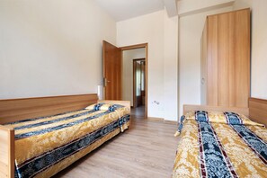 A bedroom with two wooden beds, a wardrobe, and a door leading to another room.
