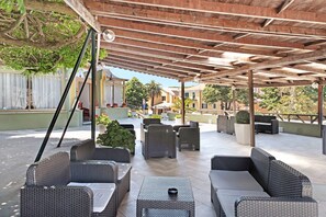 An outdoor patio with wicker furniture, a covered area, and potted plants.