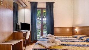 Hotelkamer met een bed, een bureau, een stoel, een televisie en uitzicht op groen.