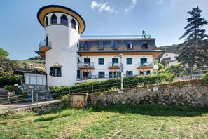 Ein großes, mehrstöckiges Gebäude mit einem zylindrischen Turm, Balkonen und einer steinernen Stützmauer.