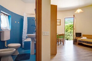 A bathroom with a toilet, sink, and shower. There is a bed with a TV and a balcony with a view.