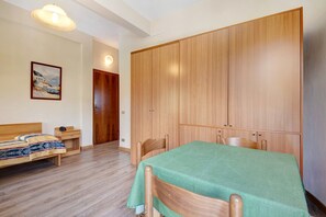 A room with a bed, a table with a green tablecloth, wooden wardrobes, and a painting on the wall.