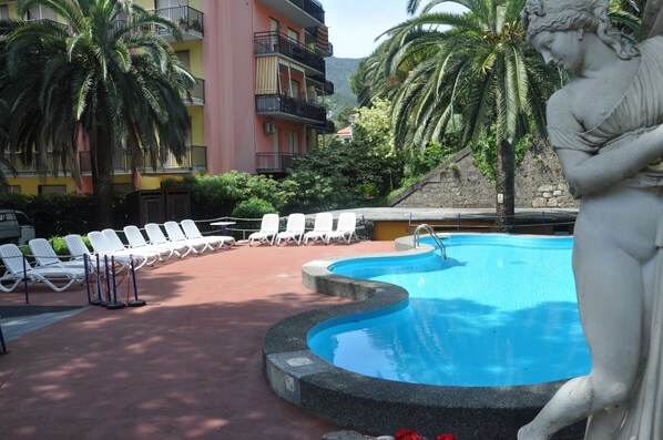 A swimming pool with lounge chairs, a statue, and a building with balconies.