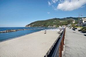 Ein Strand mit gepflastertem Gehweg, einem Rettungsturm und Gebäuden im Hintergrund.