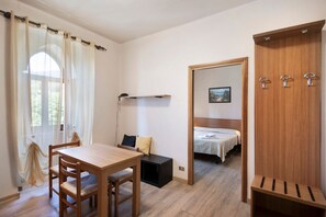 Um quarto com uma mesa de madeira, cadeiras, uma cama, um guarda-roupa e um espelho.