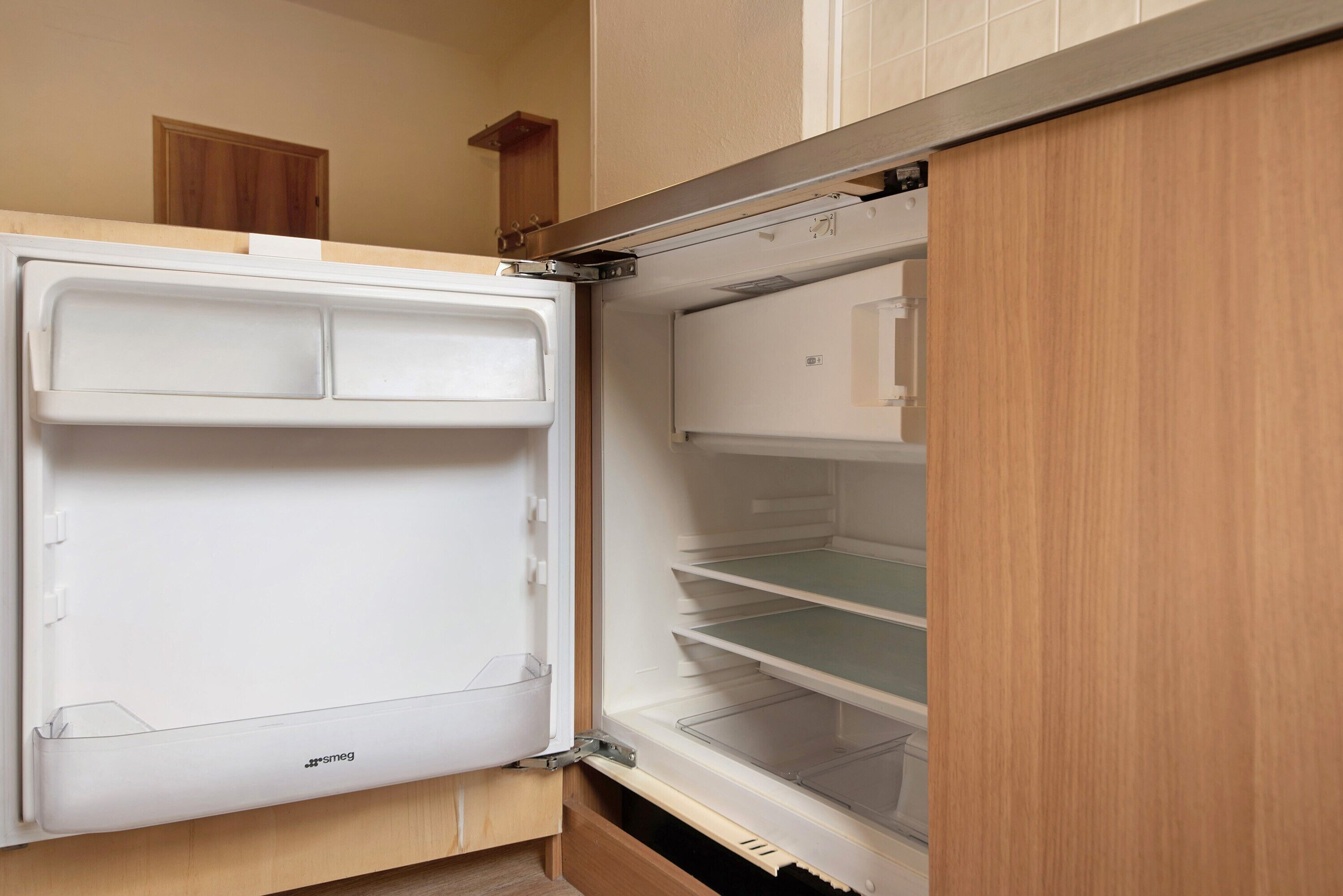 A compact kitchen with a built-in refrigerator, a wooden cabinet, and a small wooden shelf.