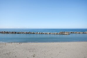 Ein Strand mit einem steinernen Wellenbrecher und ruhigem Wasser.