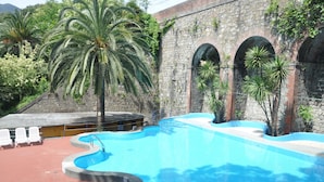 A swimming pool with a stone wall, palm trees, and white lounge chairs. - Apartment Bilocale Moneglia 31 close to the Beach with Shared Pool & Wi-Fi (Moneglia)