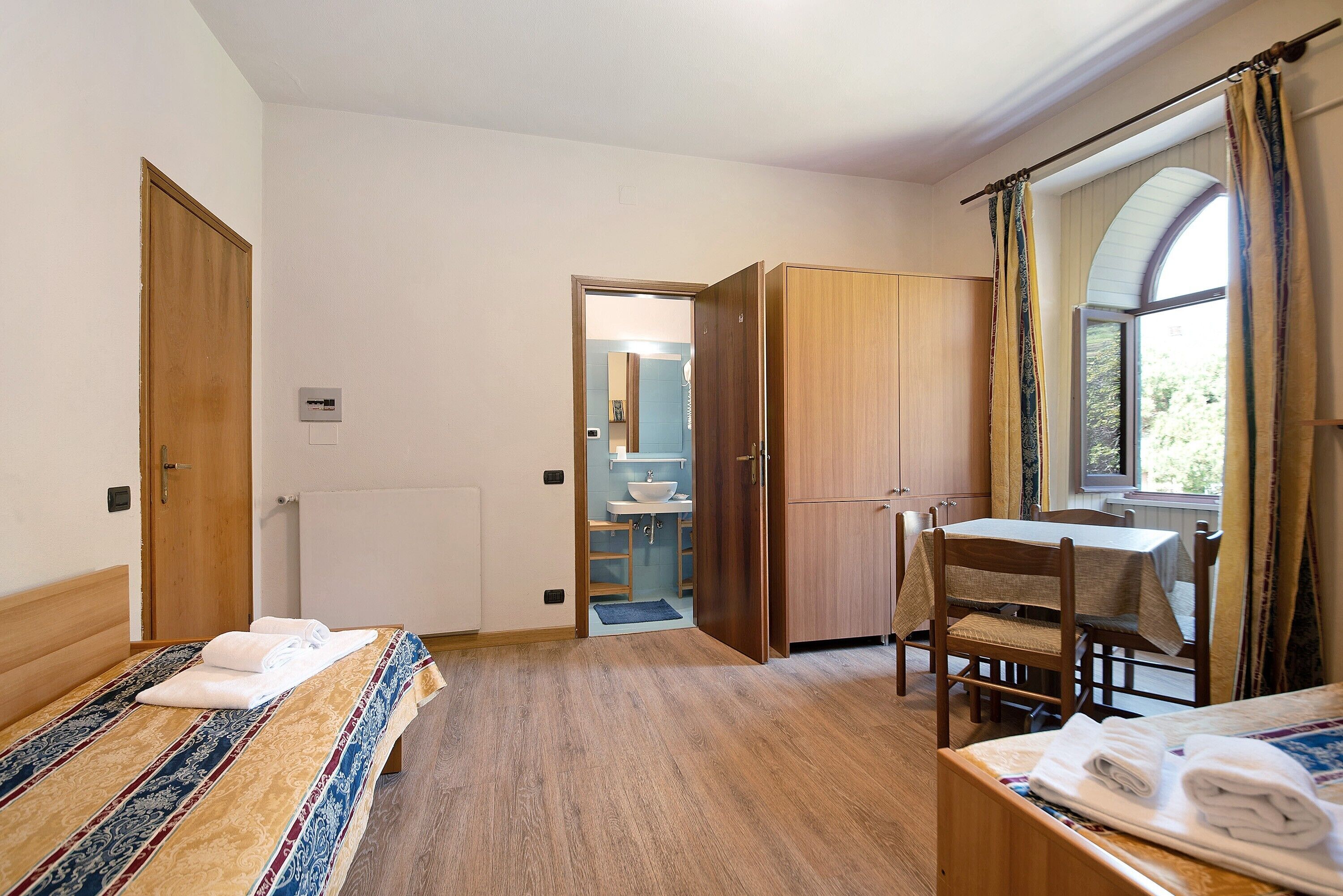 Une chambre à coucher avec un lit, un bureau et une chaise. Il y a une fenêtre avec des rideaux et une vue sur l’extérieur.