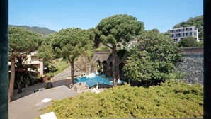 A pool area with trees and a stone wall, surrounded by greenery and a building in the background. - Apartment Bilocale Moneglia 31 close to the Beach with Shared Pool & Wi-Fi (Moneglia)