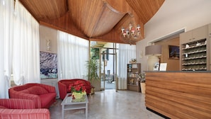 A spacious living area with a red sofa, a coffee table with flowers, a wooden reception desk, and a view through a glass door. - Apartment Bilocale Moneglia 31 close to the Beach with Shared Pool & Wi-Fi (Moneglia)