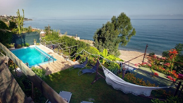 Ein Pool mit Liegestühlen, einer Hängematte und Blick auf das Meer.