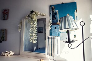 Una habitación con un espejo, una lámpara y un cuadro de un edificio azul.