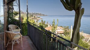 Ein Balkon mit Korbstühlen, einem Geländer und Blick auf das Meer sowie entfernte Gebäude.