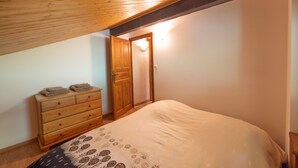 Ein Schlafzimmer mit einem Holzkasten, einem Bett mit gemustertem Überwurf und einer geneigten Decke.