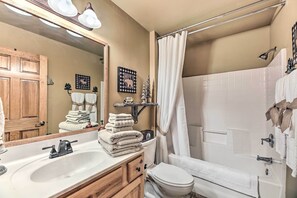 Une salle de bain avec un lavabo, des toilettes et une douche. Des serviettes sont pliées sur le lavabo et il y a un rideau de douche.