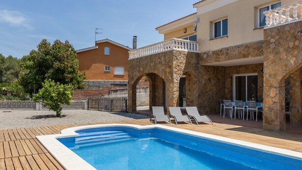 Une piscine avec des chaises longues, une terrasse en pierre et un bâtiment doté d’un balcon.