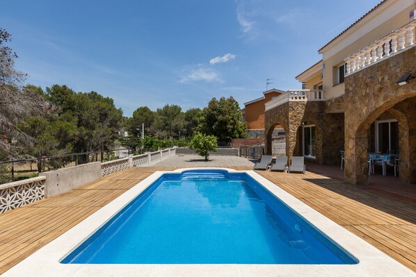 Une piscine dotée d’une terrasse en bois, d’une architecture en pierre et de mobilier d’extérieur.