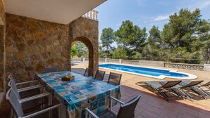 Une terrasse en pierre avec une piscine, un espace salon extérieur et une vue sur les arbres.