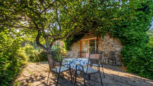 A stone building with a table and chairs under a tree.