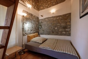 Ein Schlafzimmer mit Steinwand, einem Bett mit kariertem Überwurf, einem Nachttisch und einer Stehlampe.