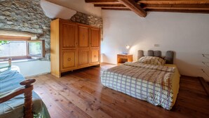A bedroom with a wooden bed, a wardrobe, a stone wall, and a window.