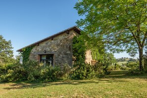 Un bâtiment en pierre doté d’un toit en pente, entouré de verdure et surplombé d’un ciel dégagé.