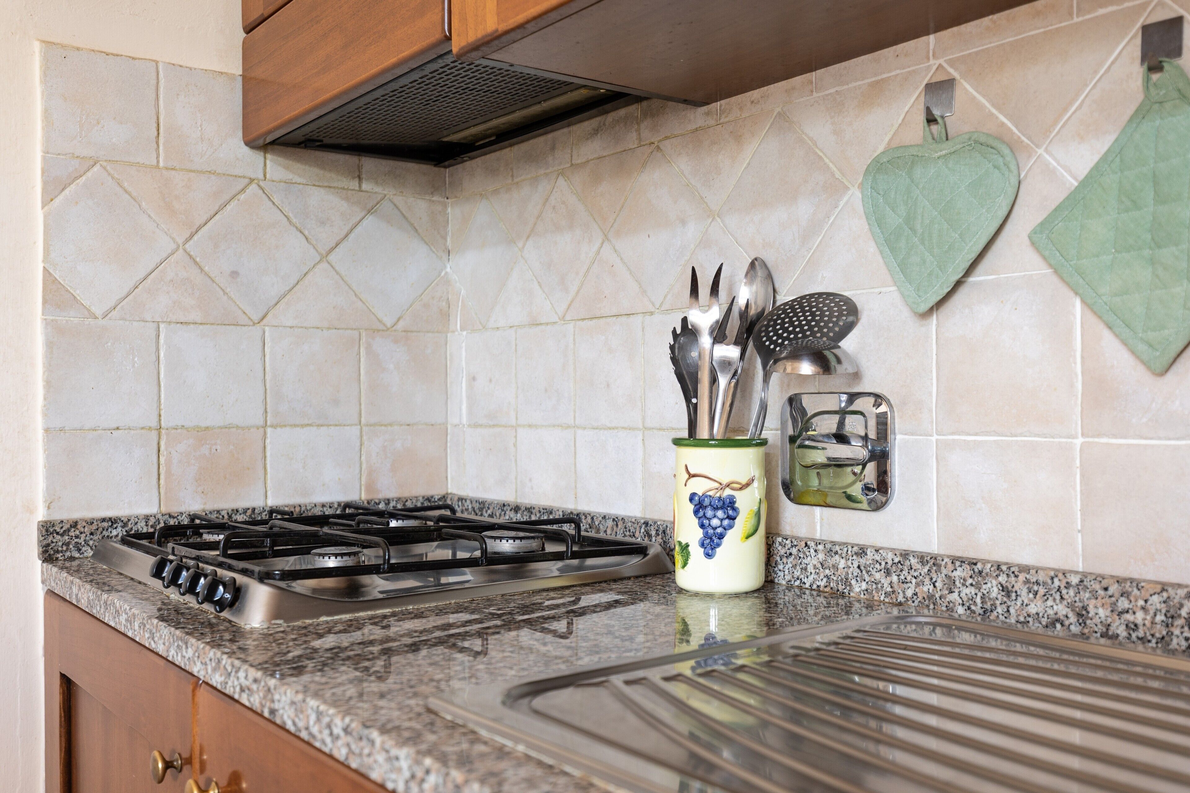 A kitchen with a gas stove, granite countertop, and a backsplash with diamond-patterned tiles.