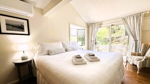 A hotel room with a large bed, a bedside table with a lamp, a chair, and a window with curtains. - Sand Bar-Dog Friendly on Cooks Brook Beach (Eastham)