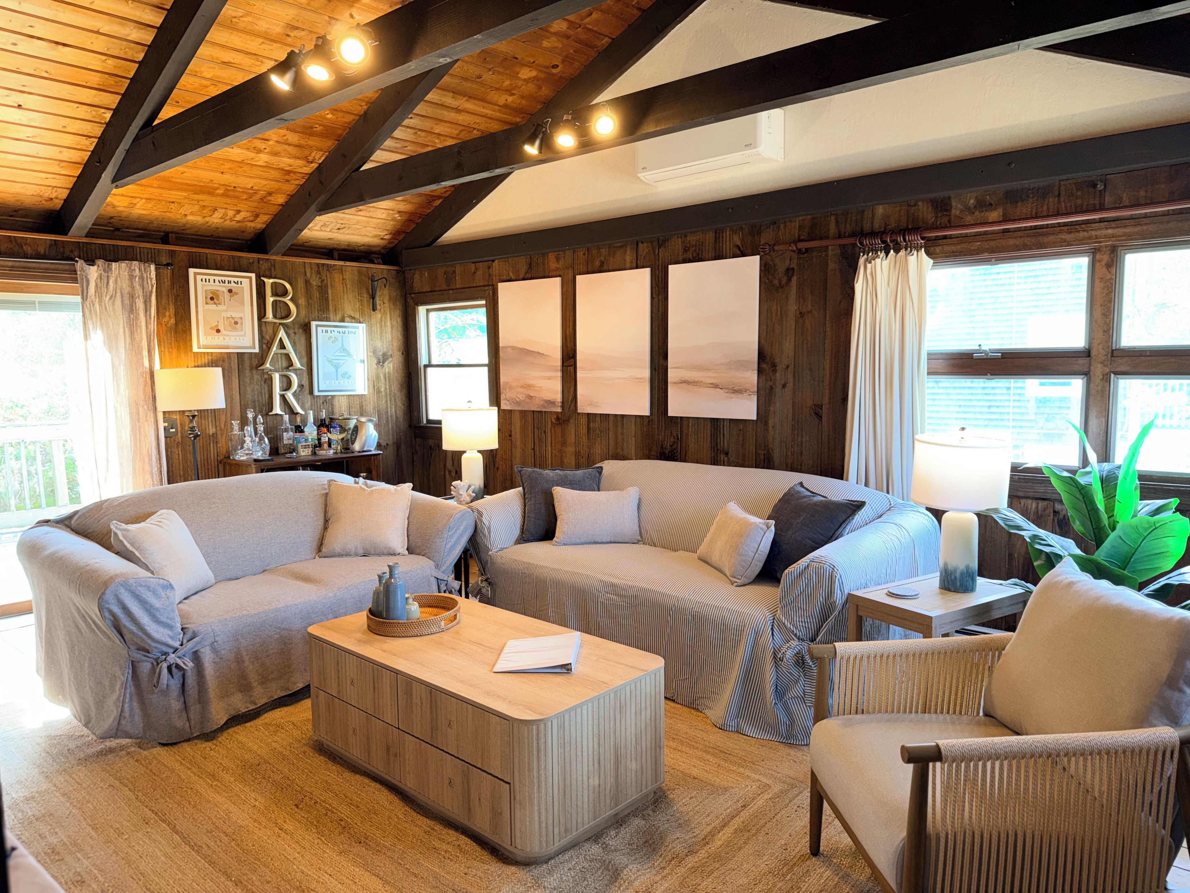 Ein gemütliches Wohnzimmer mit Holzbalkendecke, einer Sofagarnitur, einem Couchtisch und einer Bar mit einer Lampe und dekorativen Gegenständen.