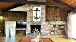 A cozy living room with a brick fireplace, a wooden coffee table, and a bookshelf. - Sand Bar-Dog Friendly on Cooks Brook Beach (Eastham)