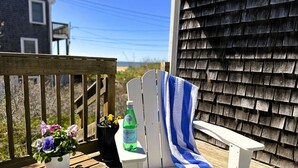 A white Adirondack chair with a blue and white striped towel, a bottle of Pellegrino water, and a potted plant with purple flowers on a wooden deck. - Sand Bar-Dog Friendly on Cooks Brook Beach (Eastham)