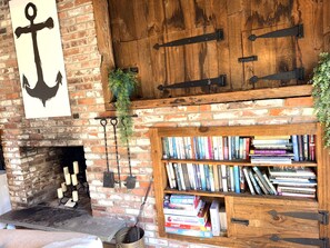 Una chimenea de ladrillo con un candelabro colgante, una estantería llena de libros y una puerta de madera con tiradores de metal.