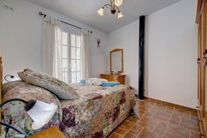 Ein Schlafzimmer mit einem Bett, einem Schminktisch, einem Spiegel, einem Fenster mit Vorhängen und einem Fliesenboden.