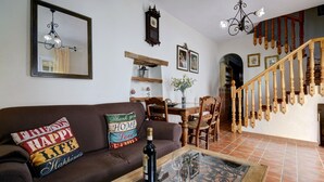 Un salon avec un canapé marron, une table basse en verre sur laquelle se trouvent une bouteille et des verres, un escalier en bois et un coin repas avec des chaises et une table.