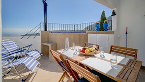 Un balcon avec une table dressée pour deux personnes, une chaise, une bouteille et un panier de fruits.