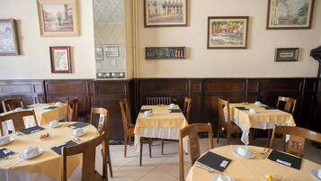 Un comedor con mesas dispuestas para el desayuno, cuadros en las paredes y sillas de madera.