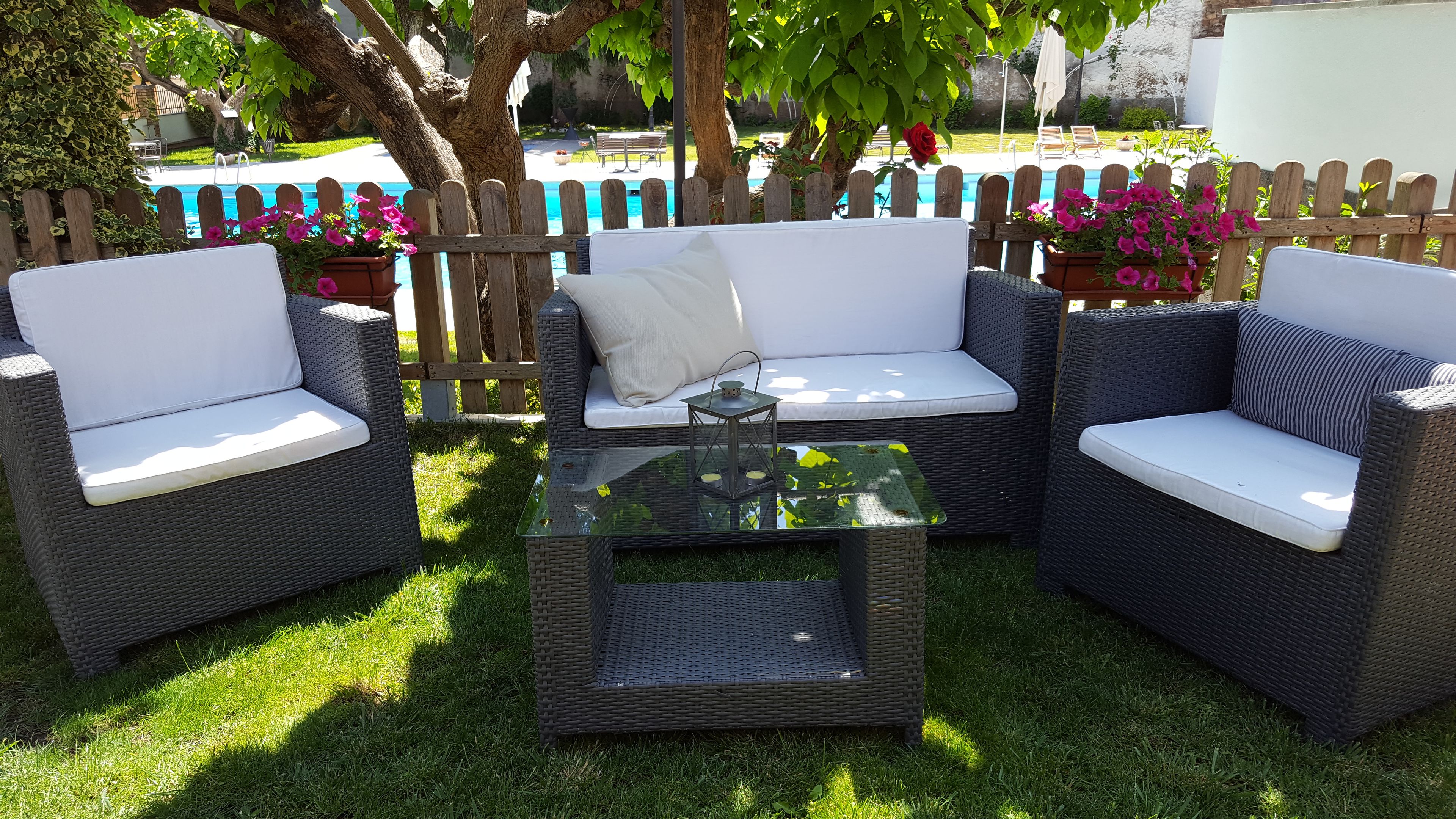 A patio area with wicker furniture, a glass-top table, and a view of a swimming pool.