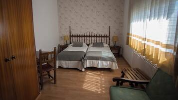 A room with two beds, a wooden bench, a chair, and a radiator.
