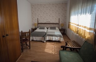 A room with two beds, a wooden bench, a chair, and a radiator.