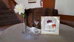 Una mesa con un jarrón de flores blancas, un cuadro con la imagen de dos flores y tres copas de vino.