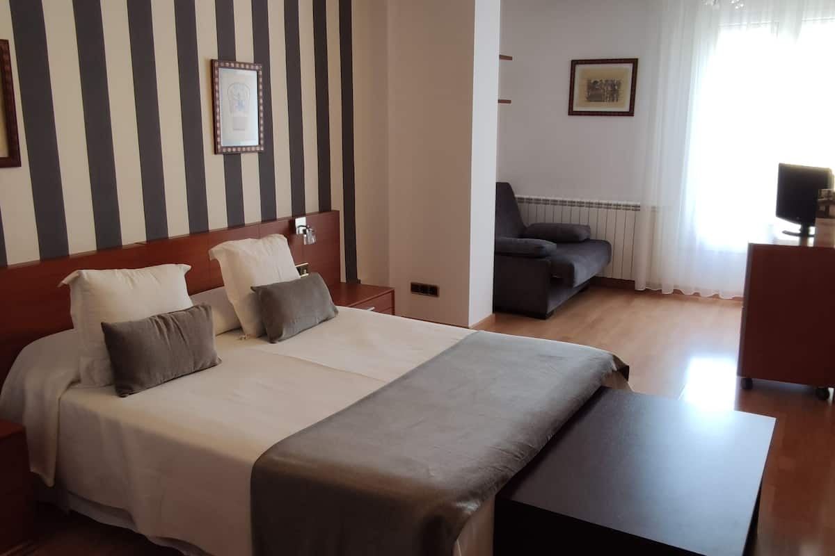 A hotel room with a large bed, a sofa, a desk, and a chair.