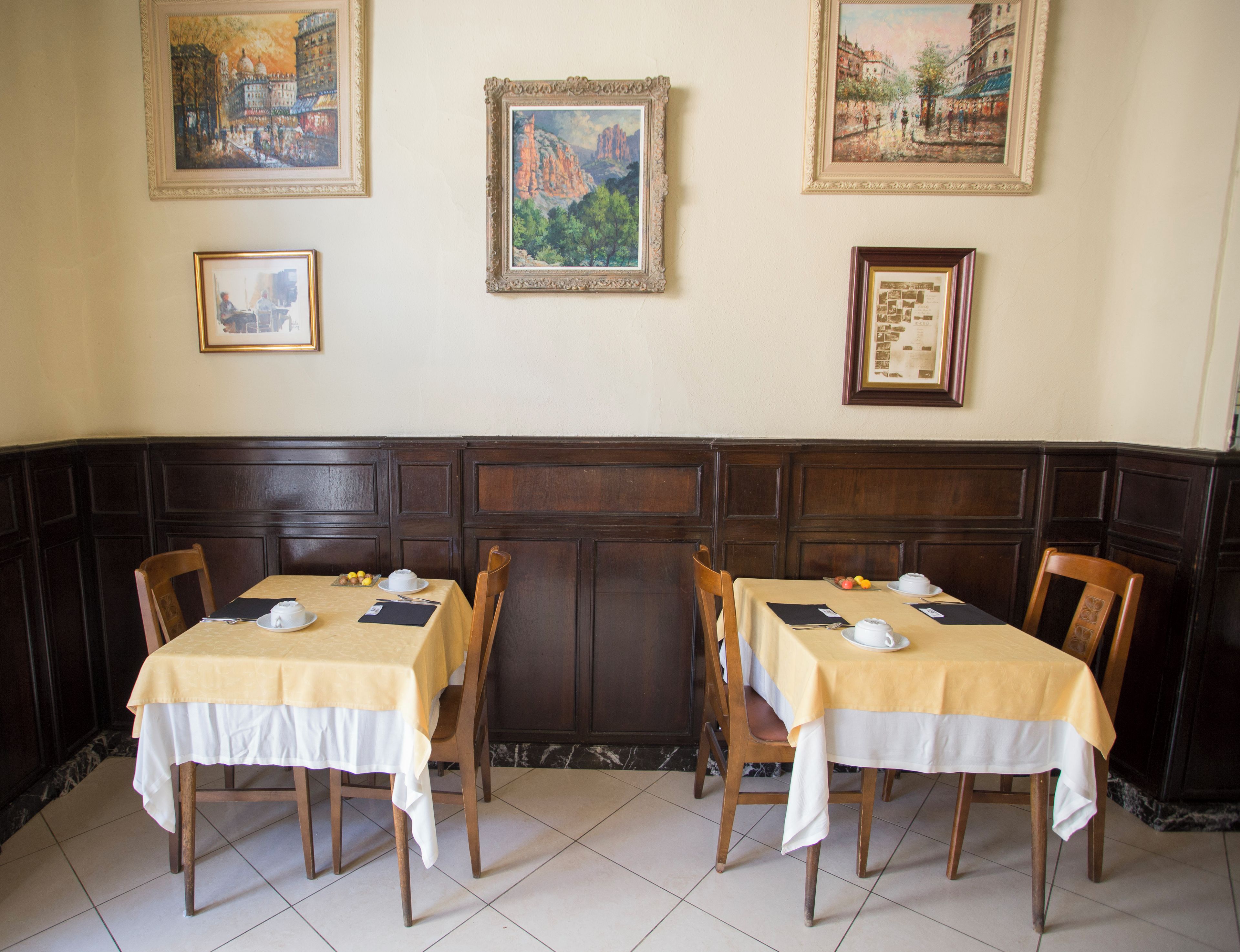 A dining area with two tables, each set with white tablecloths and chairs, and framed artwork on the walls.